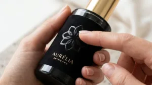 Close Up Of A Consumer's Hand Touching The Raised Spot Uv Texture On A Luxury Cosmetic Bottle Label In A Bright Studio Setting.